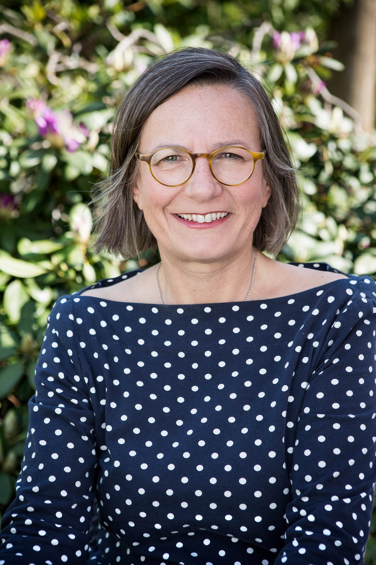 Annemarie Stoltenberg Frau mit blauer, weiß gepunkteter Bluse und Brille lächelt in die Kamera