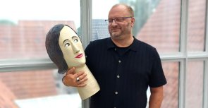 Gezeigt wird ein Mitarbeiter, der eine Pappmachefigur im Arm hält
