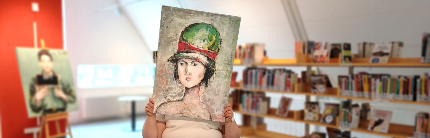 Eine Mitarbeiterin hält sich ein Portraitbild vor ihr Gesicht, zu sehen ist auf dem Bild eine Frau mit Hut