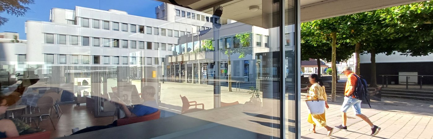 Gezeigt wird ein Blick in die Bibliothek Rheda, in den Glasscheiben spiegelt sich das Rathaus Rheda