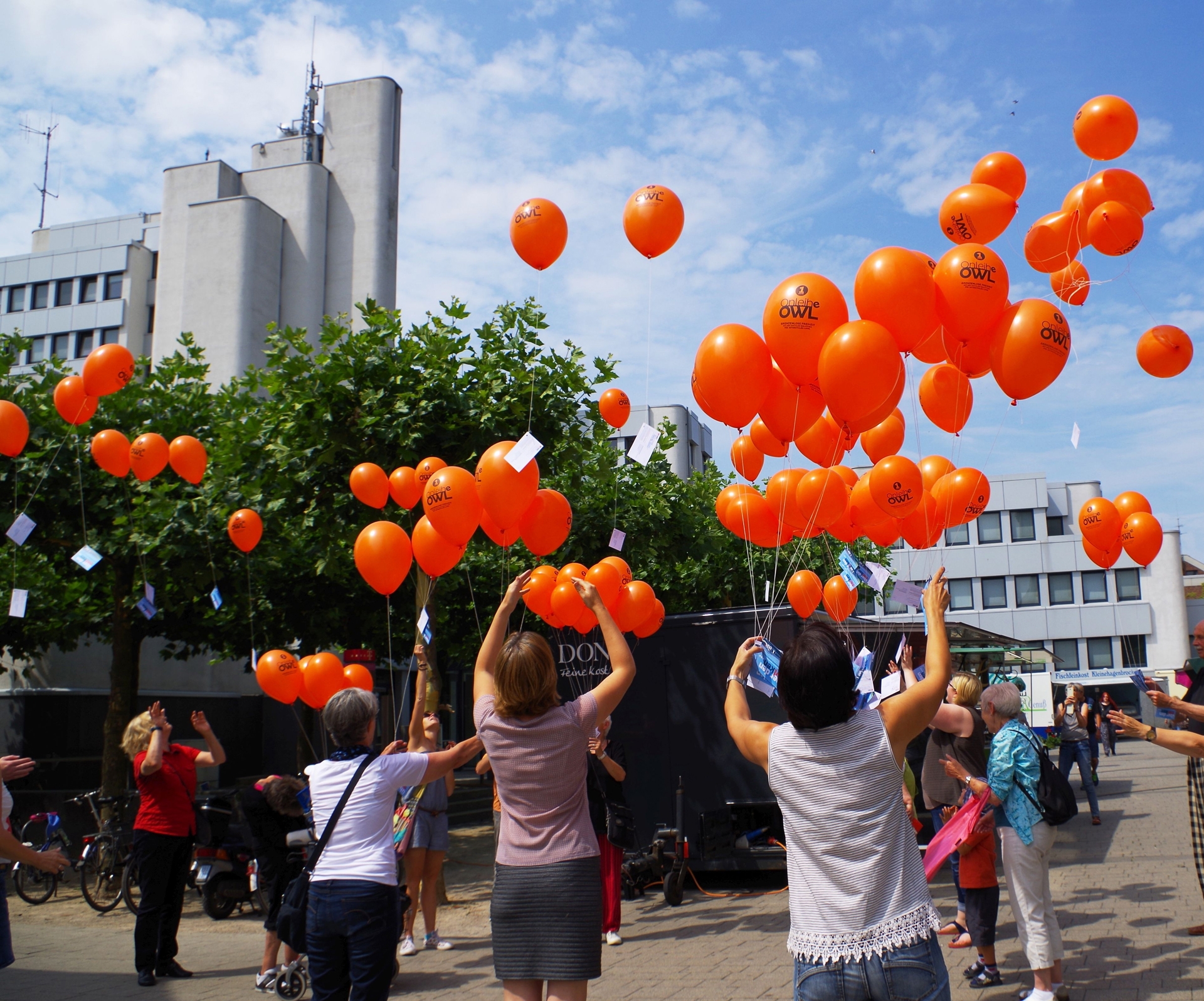 Gezeigt werden aufsteigende, orangene Luftballons vor dem Rathaus Rheda