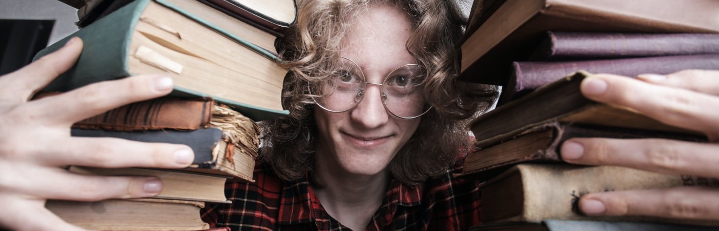 Ein junger Mann schaut durch zwei Bücherstapel