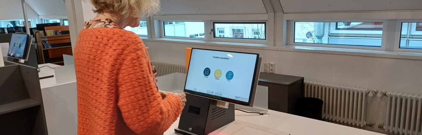 Gezeigt wird eine Mitarbeiterin an den Selbstverbuchern