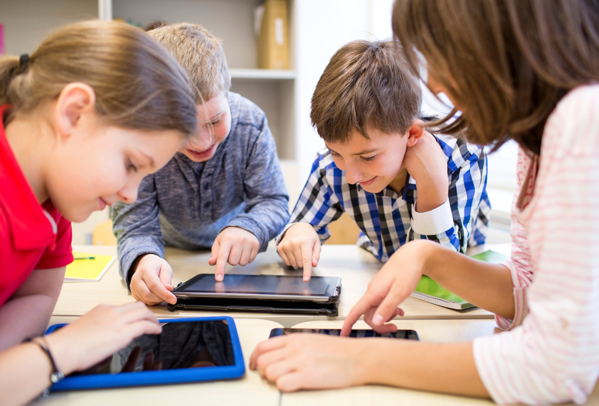 Vier Kinder schauen auf auf einem Tisch liegende Tablets