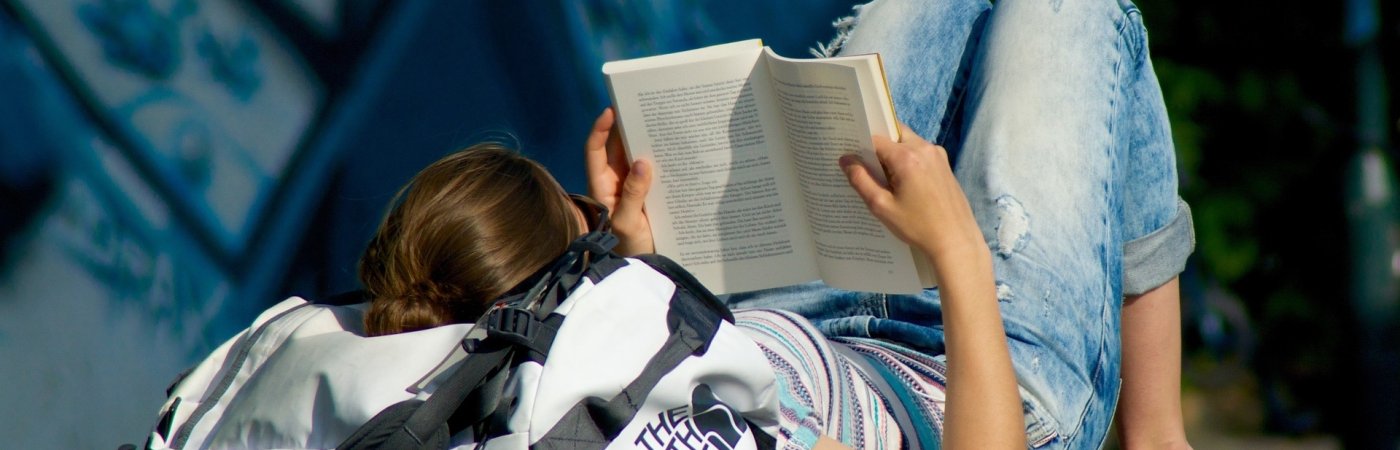 Gezeigt wird eine auf dem Rücken liegende, lesende junge Frau