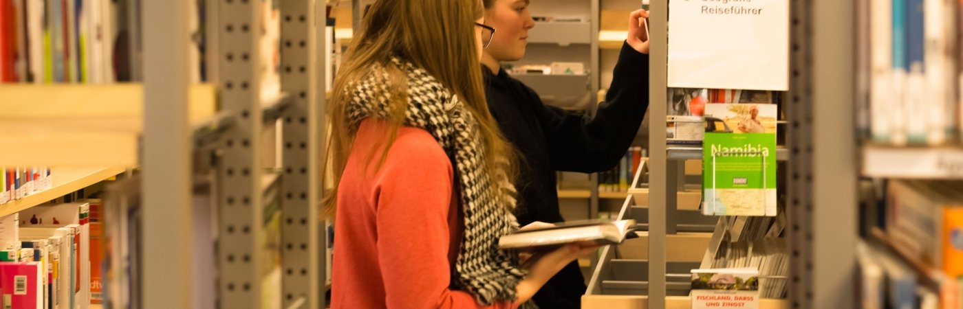 Zwei Jugendliche stehen stöbernd an einem Bücherregal