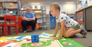 Gezeigt wird ein auf einem Spielteppich kniender Junge