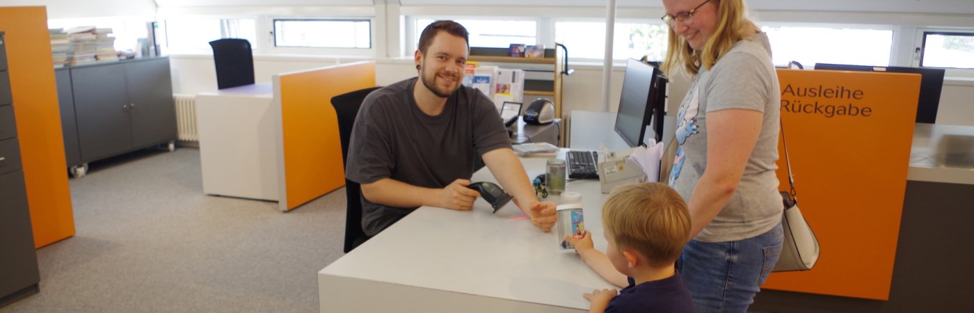 Gezeigt wird eine Familie an der Ausleihtheke