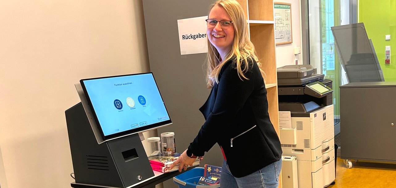 Gezeigt wir eine Mitarbeiterin an einer Selbstverbuchungsstation