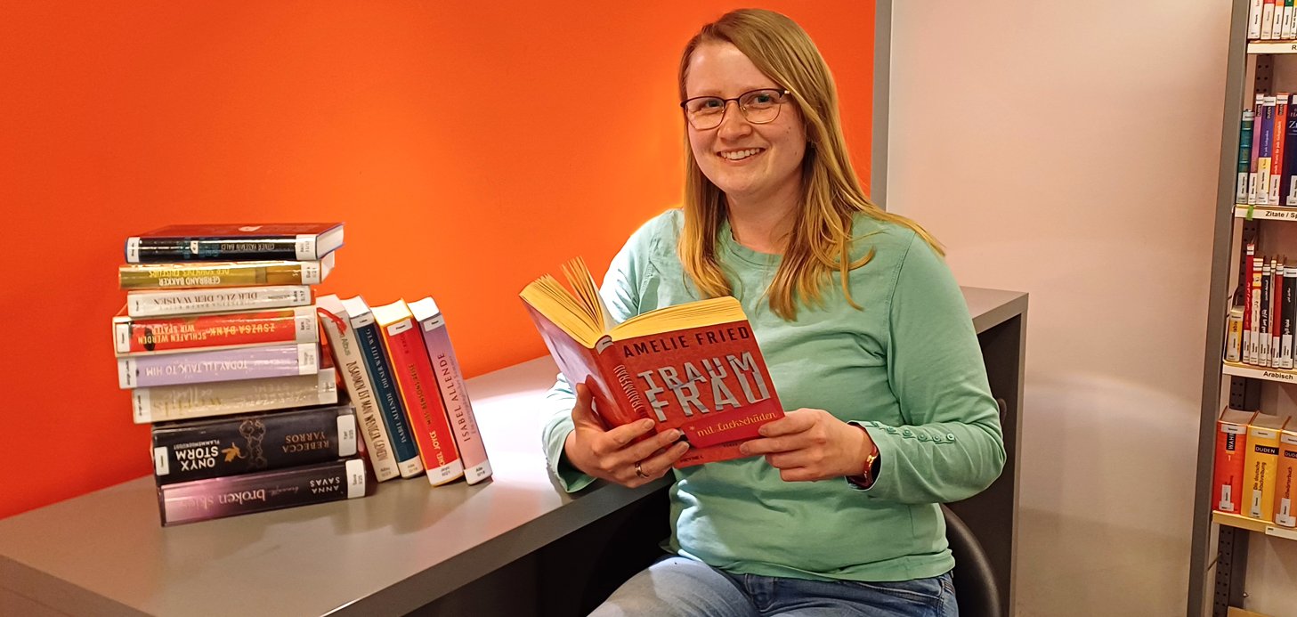 Gezeigt wird eine Mitarbeiterin der Bibliothek, ein Buch in den Händen haltend