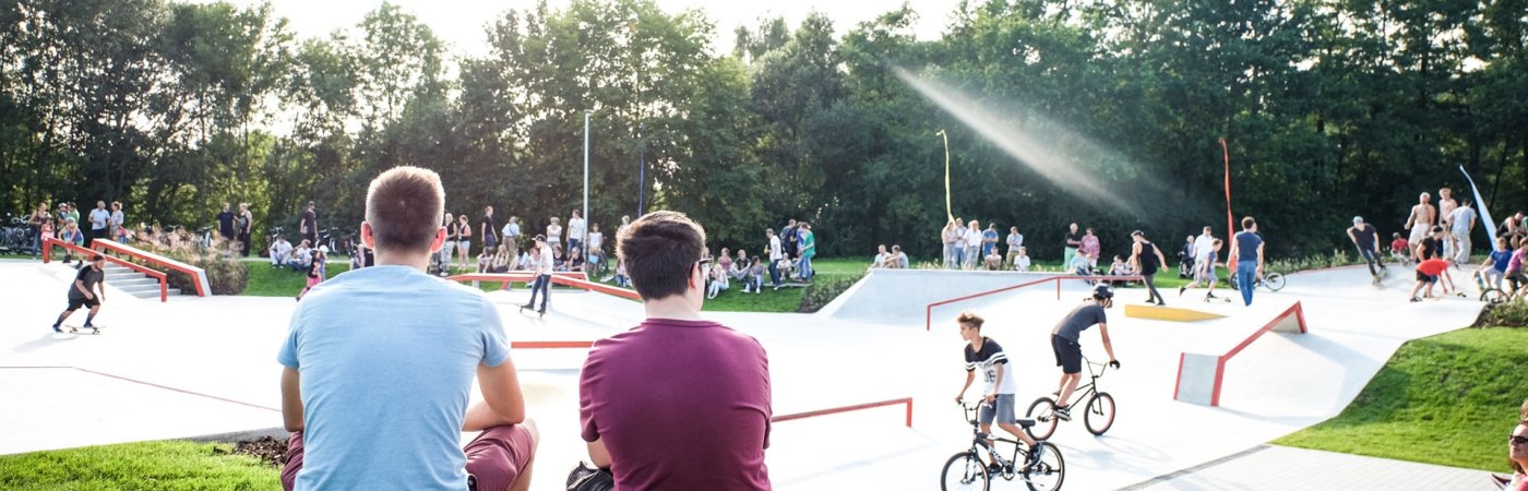 Jugendliche sitzen auf einer Bank und schauen auf den Skaterpark im Flora Park
