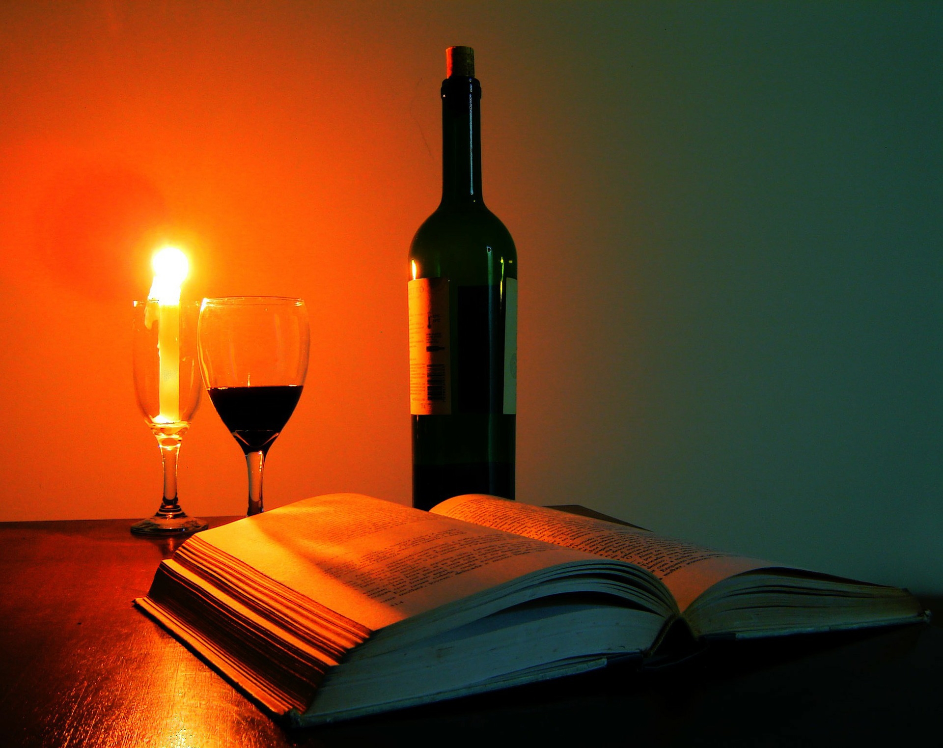 Gezeigt wird ein Buch mit Weinglas im Kerzenschein