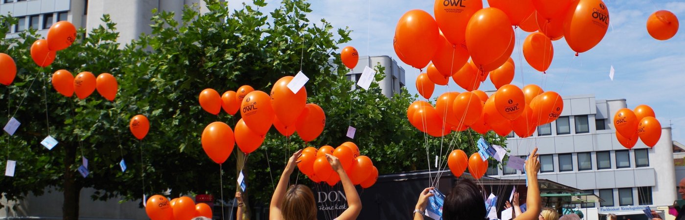 Luftballons vor dem Rathaus Rheda Menschen lassen orangene Lufballons in die Luft steigen, im Hintergrund ist das Rathaus in Rheda zu sehen